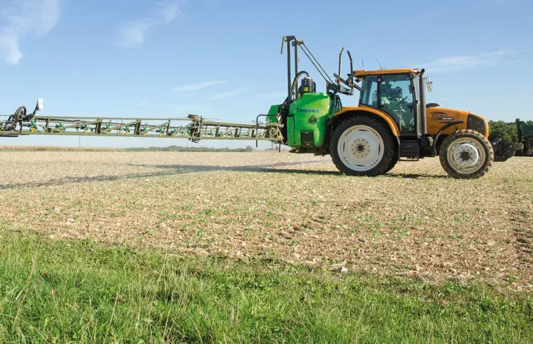Un pulvérisateur dans une parcelle agricole bordée par une bande herbeuse.