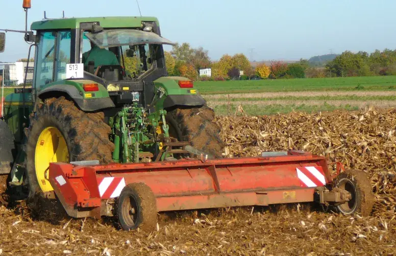 Dans un champ, un tracteur broie des résidus de maïs avant le semis d'un blé.