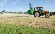 Un pulvérisateur dans une parcelle agricole bordée par une bande herbeuse.